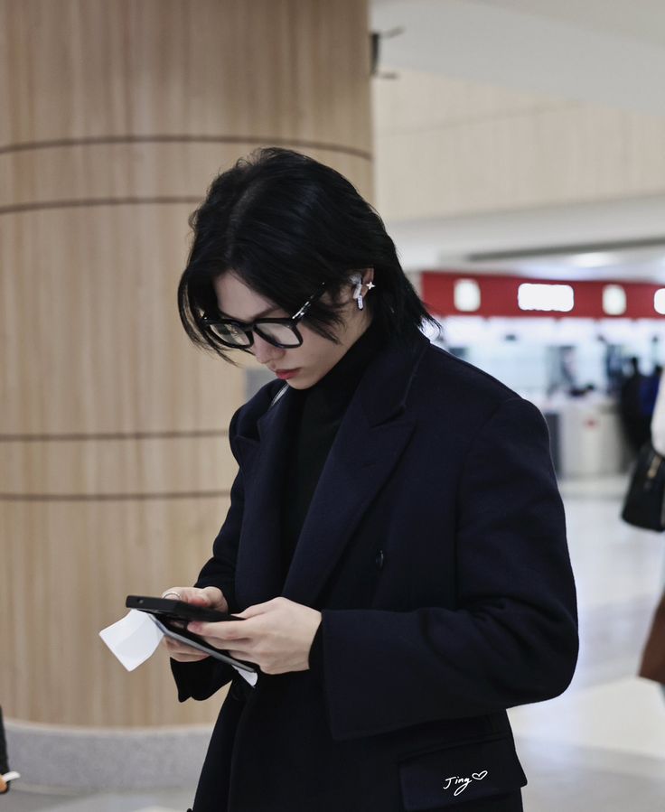 a man with black hair and glasses is looking at his cell phone in an airport