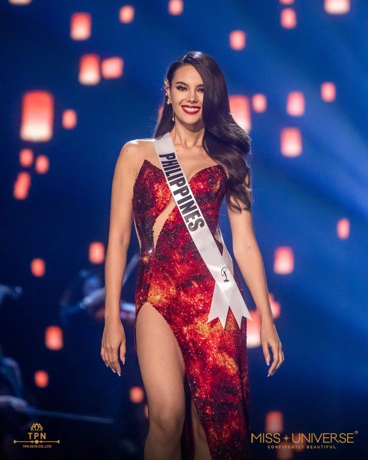 miss universe contestant wearing a red and white dress with her name on the side, standing in