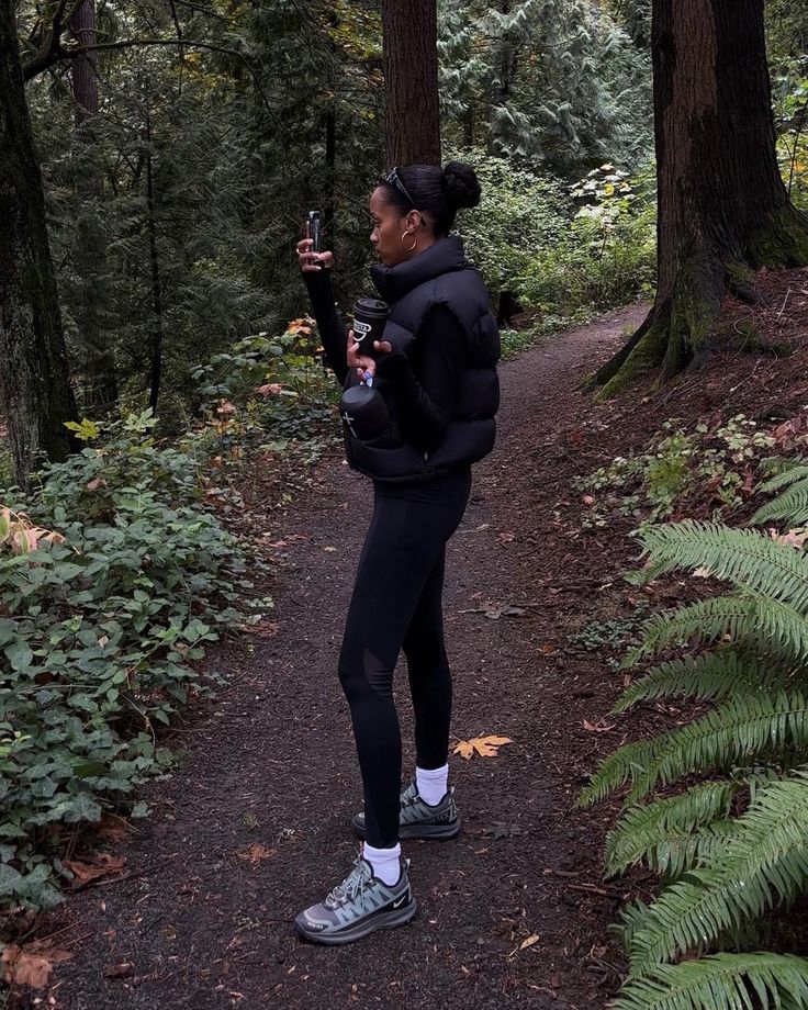 a woman standing on a path in the woods taking a photo with her cell phone