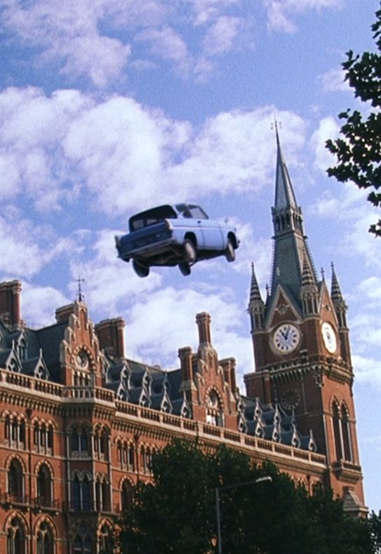 an old car is flying in the air over a large building with a clock tower