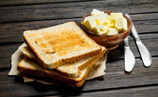 two pieces of bread with butter on them and a bowl of butter next to it