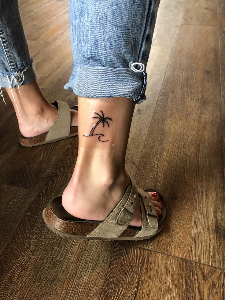 a woman's foot with a small palm tree tattoo on her left side ankle