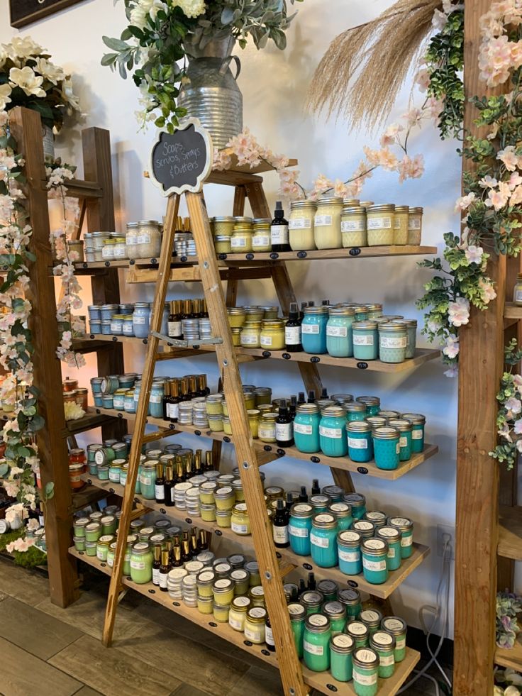 the shelves are filled with jars and candles for sale in front of a floral wall