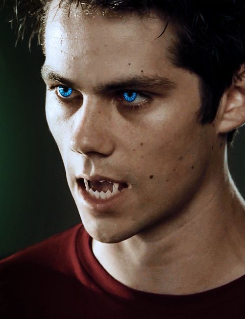 a young man with blue eyes and fangs on his face is staring at the camera