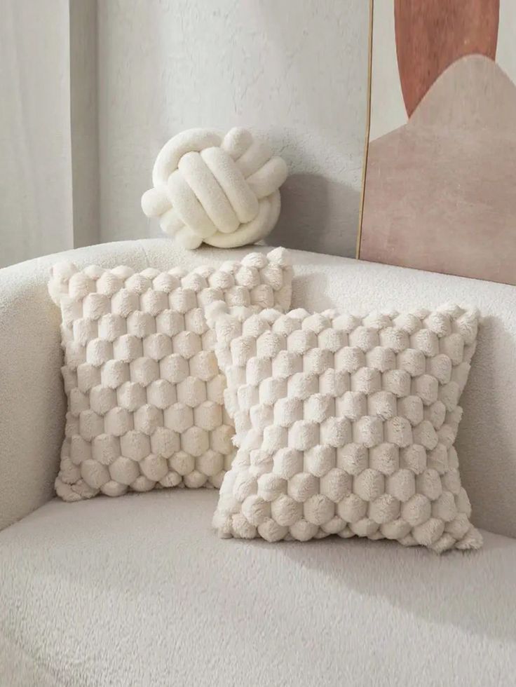 two white pillows sitting on top of a couch next to a pillow with a knot