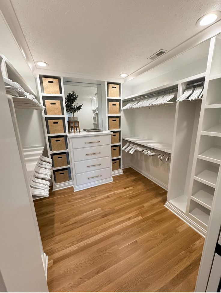 a walk in closet filled with lots of white shelves and drawers next to a wooden floor