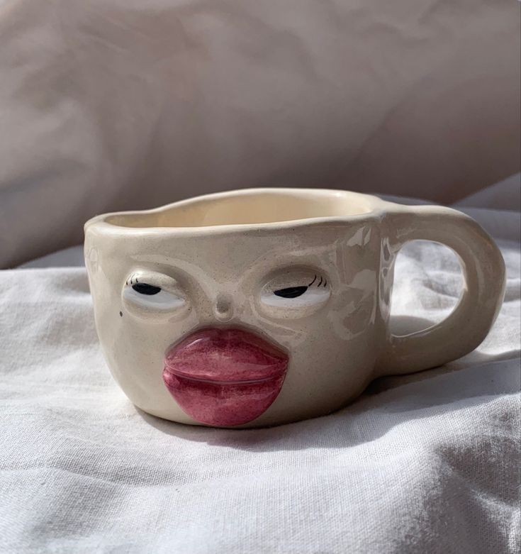 a ceramic cup with a face painted on it's side sitting on a white sheet