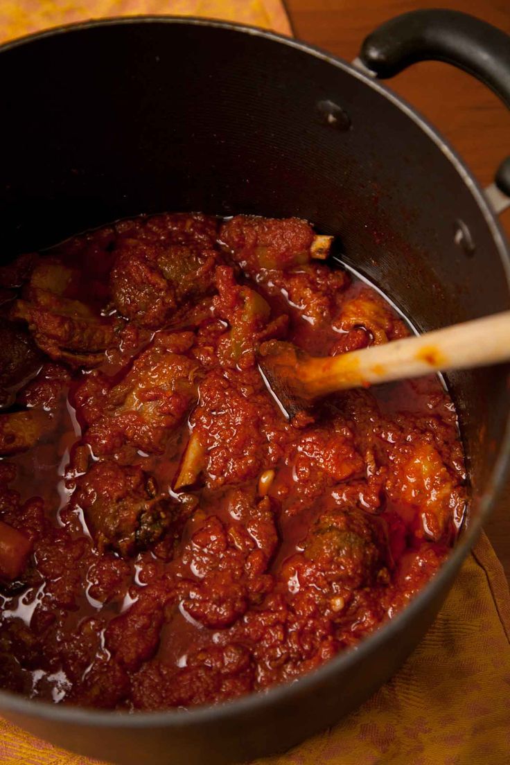 a pot filled with meat and sauce on top of a wooden table