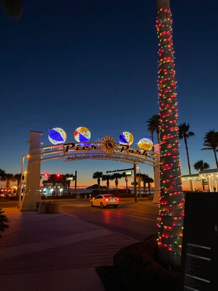 the entrance to an amusement park at night with lights on it and palm trees in the foreground