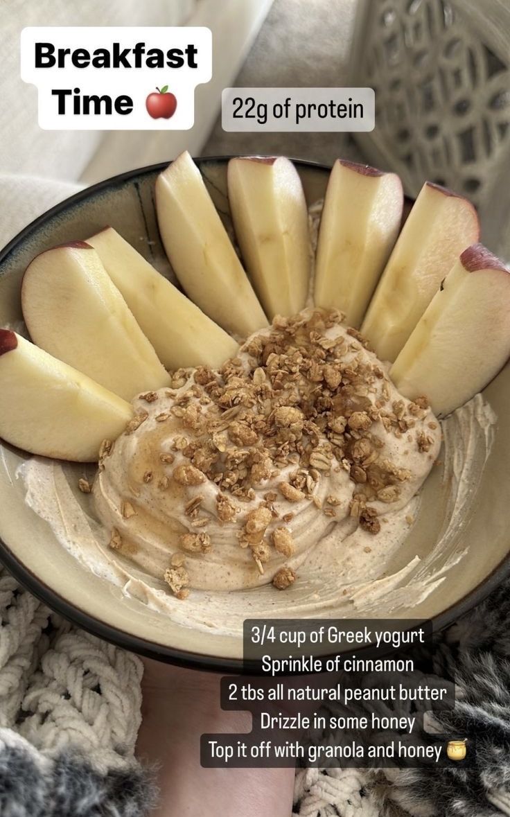 a bowl filled with apples and granola on top of a white plate next to a person's hand