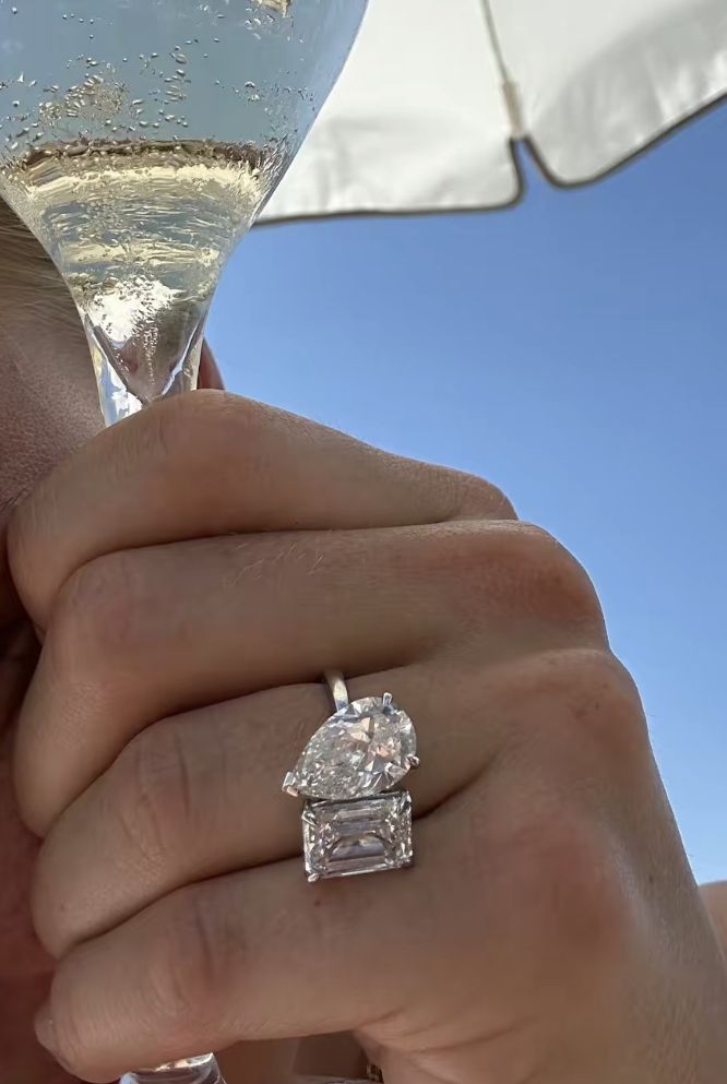 a close up of a person holding a wine glass with a diamond ring on it