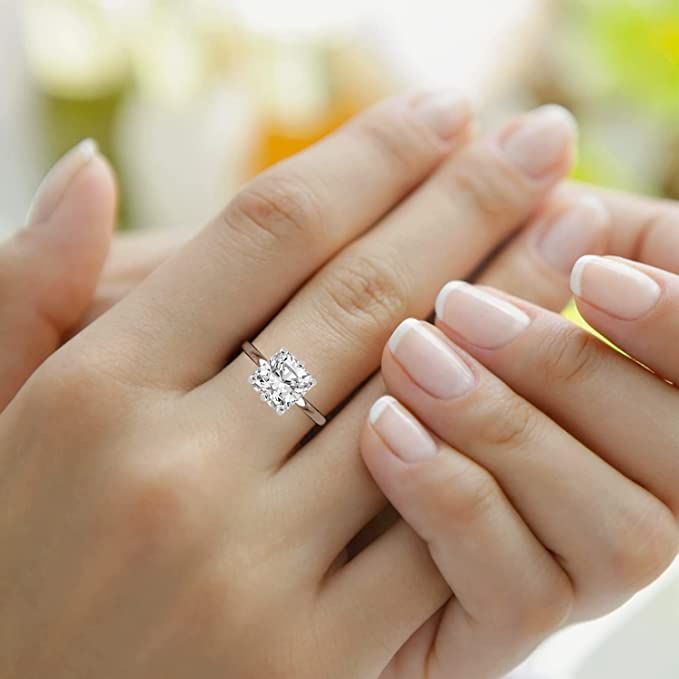 a woman's hand holding a diamond ring on top of her left hand,