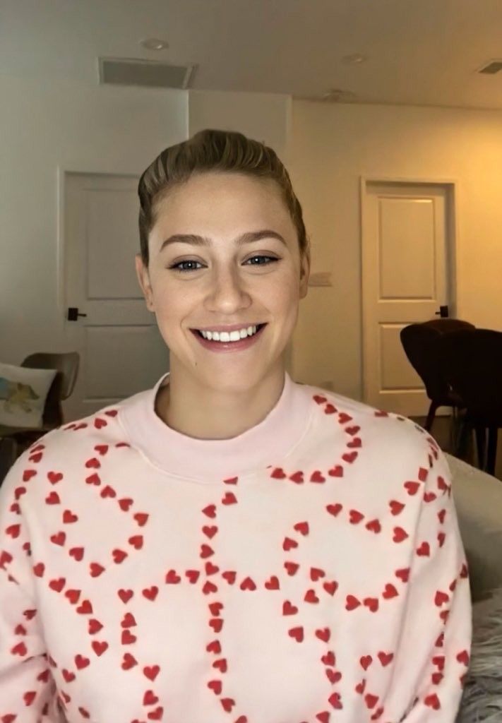 a woman wearing a red and white sweater with hearts on it smiling at the camera