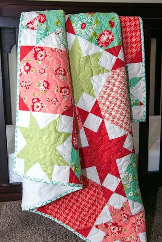 two quilts are hanging from a crib in a nursery area, one is red and the other is green