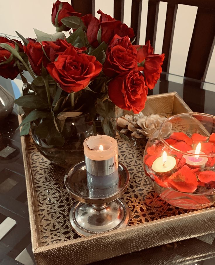 a tray with candles and roses on it sitting on a table next to a vase filled with flowers