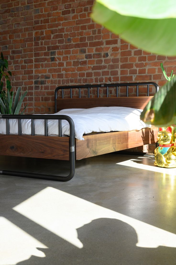 a bed sitting in the middle of a room next to a brick wall and potted plants