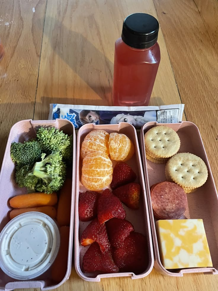 three trays filled with different types of food next to a bottle of juice and some crackers