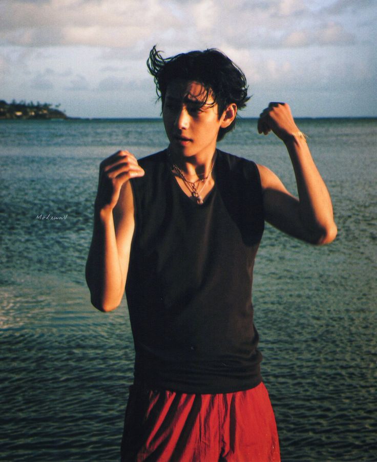 a young man standing in front of the ocean with his arms up and fists raised