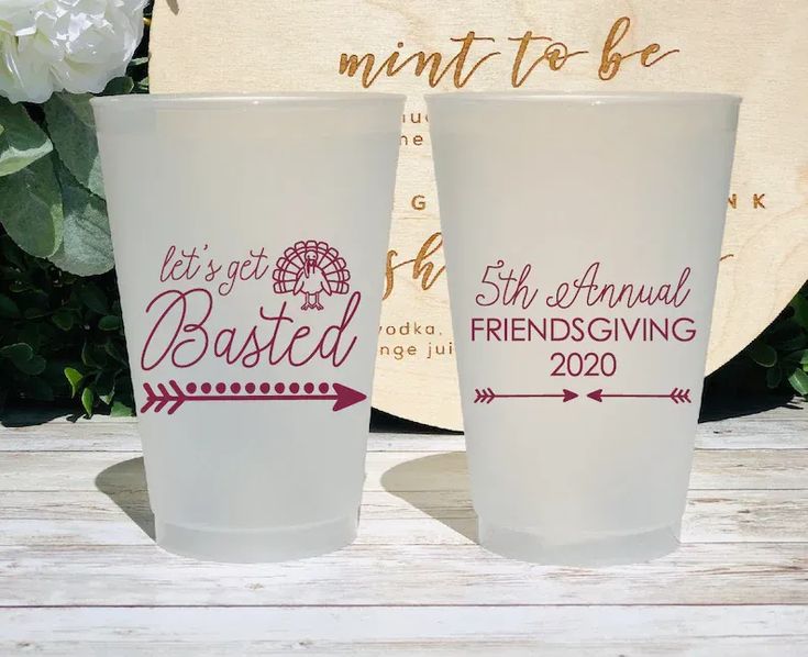 two frosted cups sitting next to each other on top of a wooden table with flowers in the background