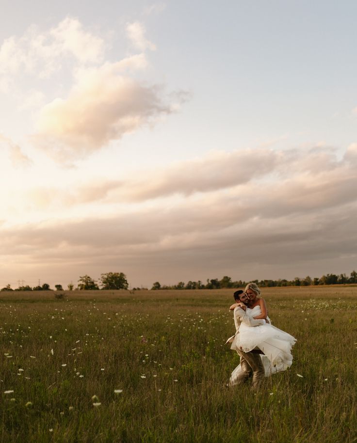 a bride and groom in a field at sunset