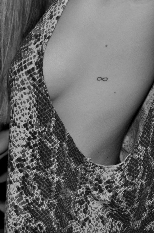 the back of a woman's chest with an infinite symbol tattoo on it