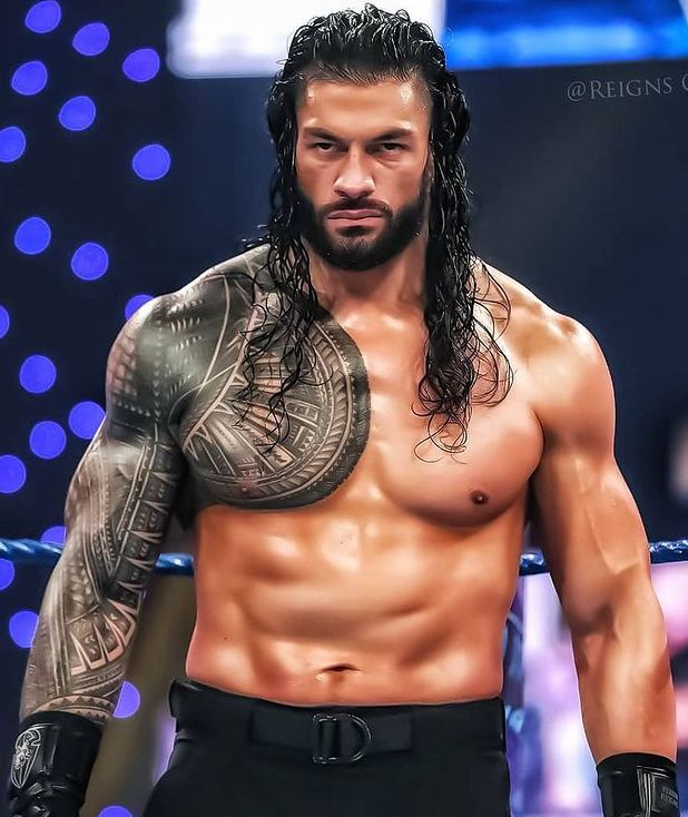 a man with long hair and tattoos on his chest standing next to a wrestling ring