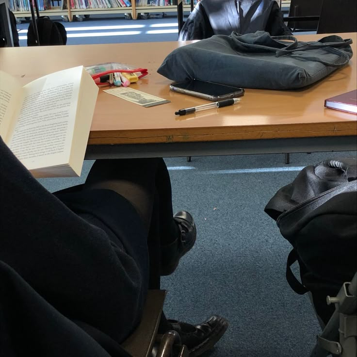 a person sitting at a table with a book in front of them and a bag on the floor