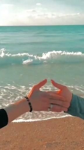 two people making the shape of a heart with their hands in front of the ocean