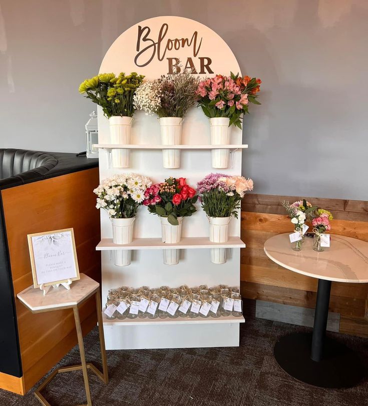 a flower shop display with flowers on the wall and small tables in front of it