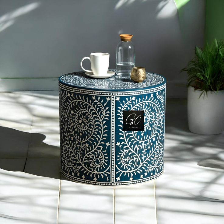 a blue and white table with a cup on it next to a potted plant