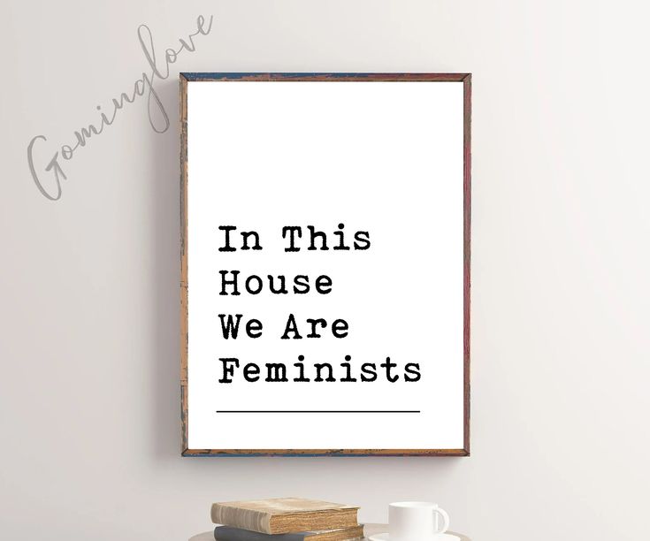 a framed poster with the words in this house we are feminists next to a stack of books