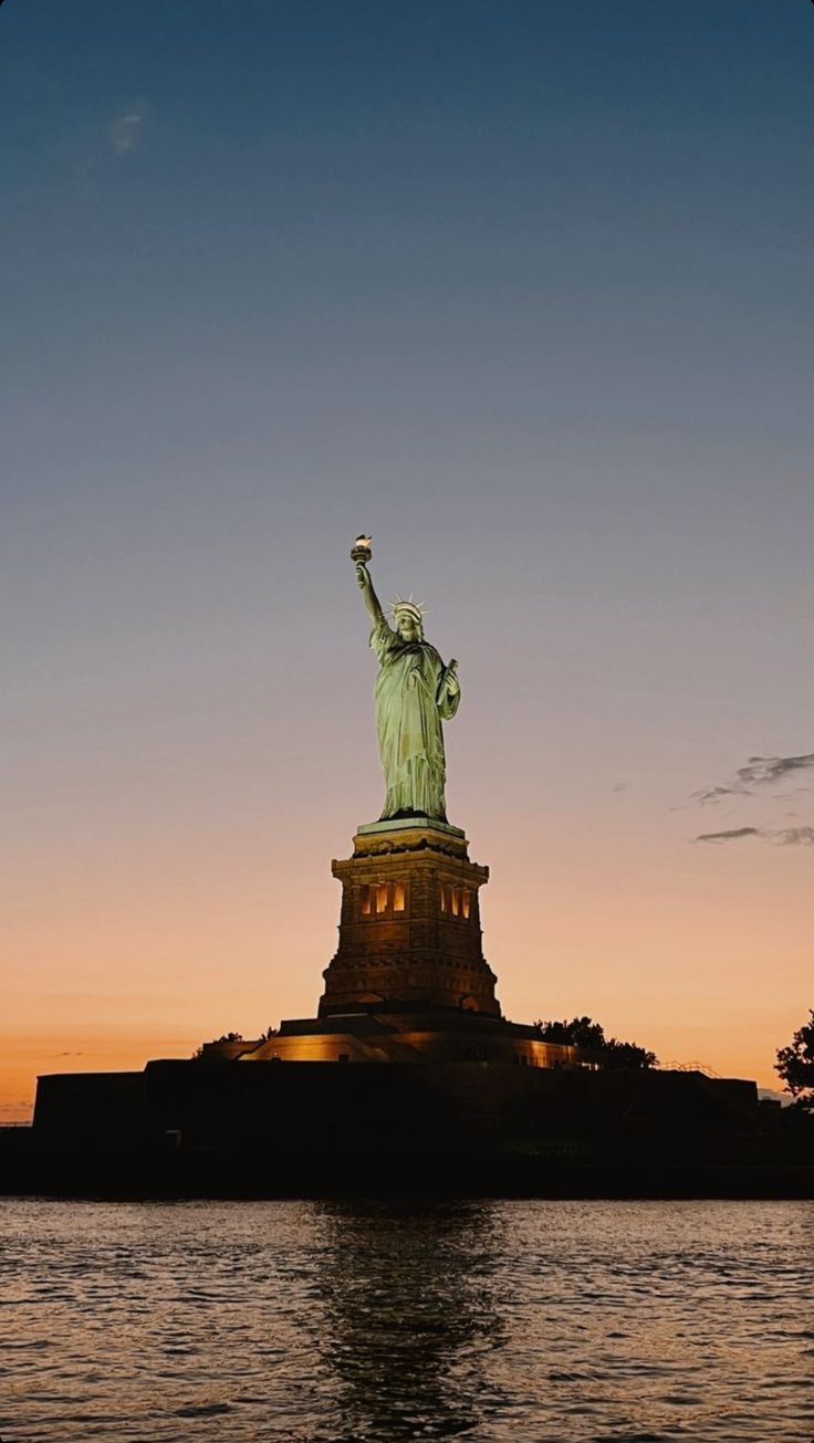 the statue of liberty is lit up at sunset