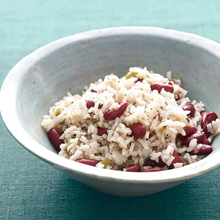 a white bowl filled with rice and beans on top of a blue tablecloth next to a spoon