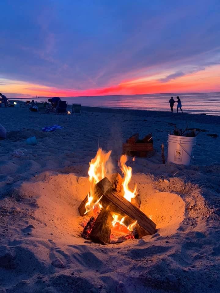 there is a fire pit on the beach with people in the background at sunset or dawn