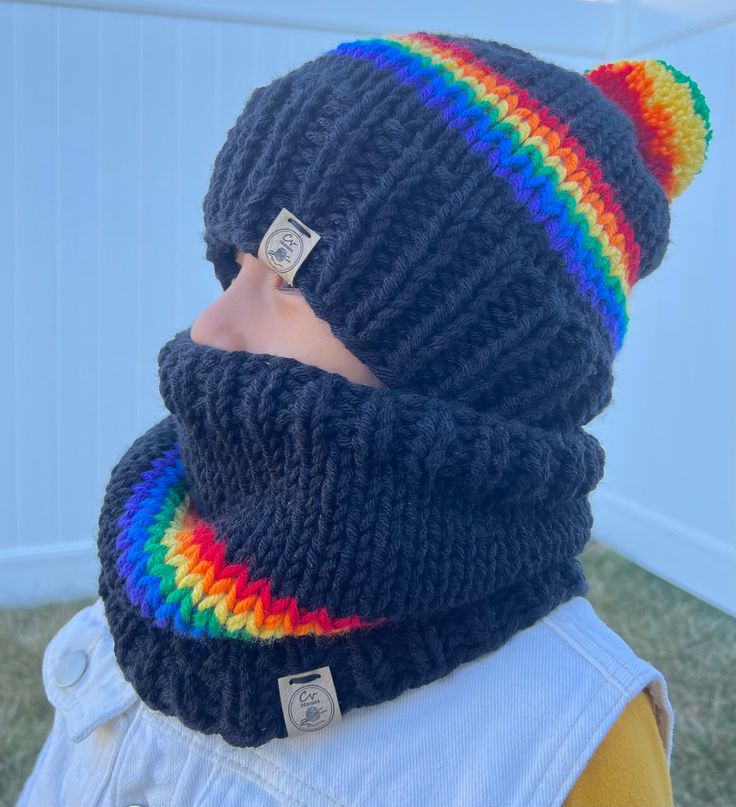 a child wearing a knitted hat and scarf with a rainbow colored cat ear tag