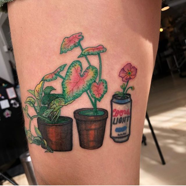 a woman's thigh with tattoos on her legs and potted plants next to a soda can