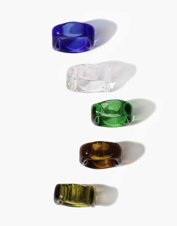 four different colored glass objects are arranged in a row on a white surface with shadows