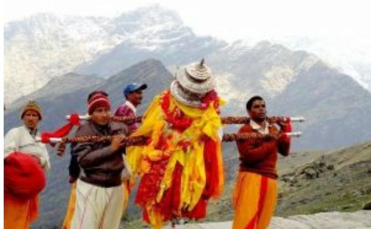 some people are standing on a hill with mountains in the background and one is holding a stick