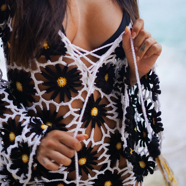 a woman wearing a crochet top with flowers on the front and back, holding a string