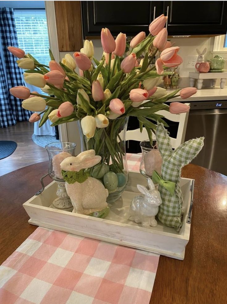 a wooden table topped with a vase filled with tulips and bunny figurines