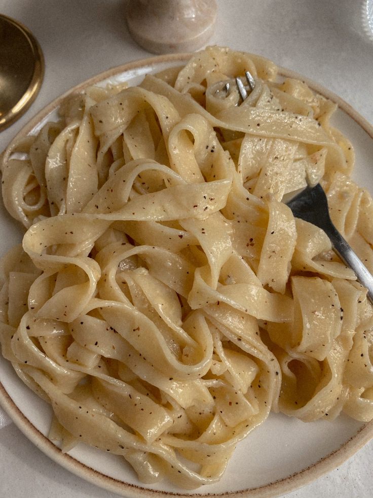 a white plate topped with pasta on top of a table next to utensils