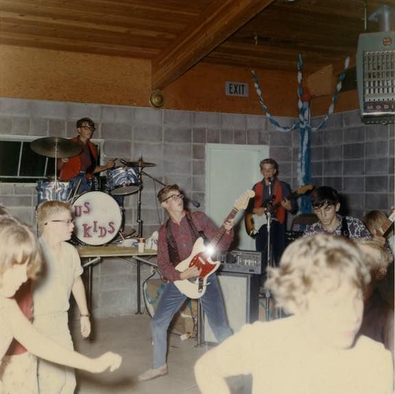 a group of people playing instruments and singing in a room with other people standing around