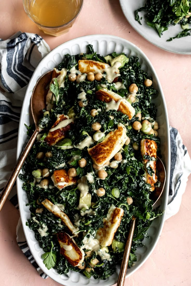 a white bowl filled with greens and chicken next to two glasses of beer on a pink table