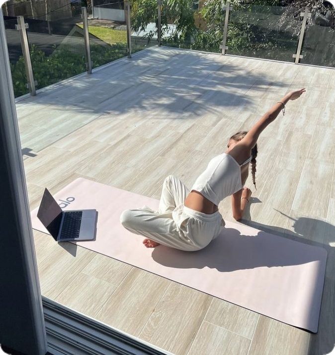 a woman is doing yoga on a mat outside with a laptop computer in front of her