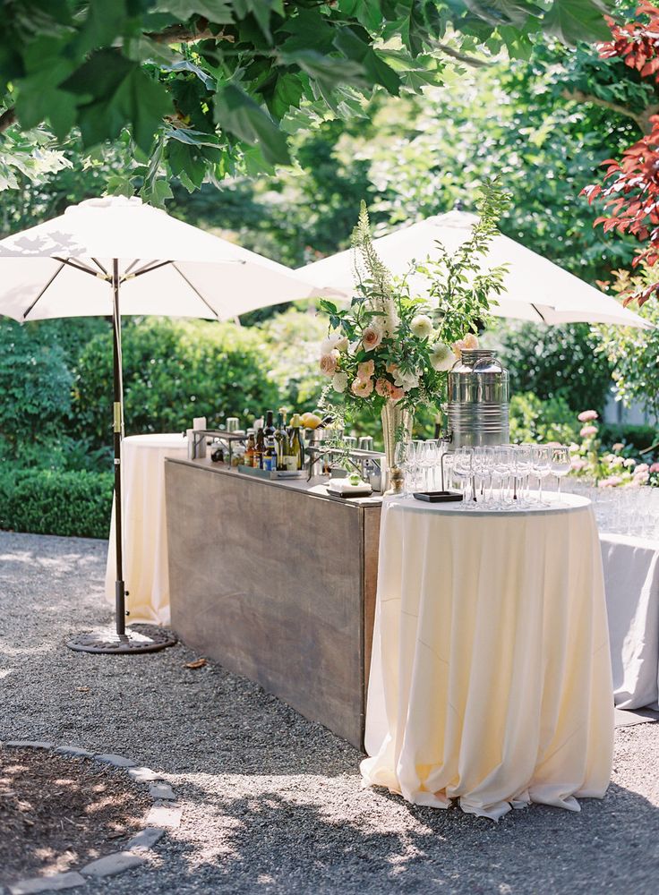 an outdoor bar set up with umbrellas and flowers on the table in front of it