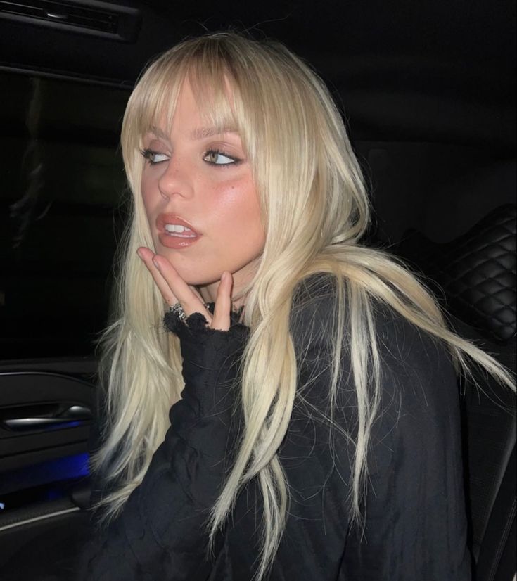 a blonde woman sitting in the back seat of a car with her hand on her chin