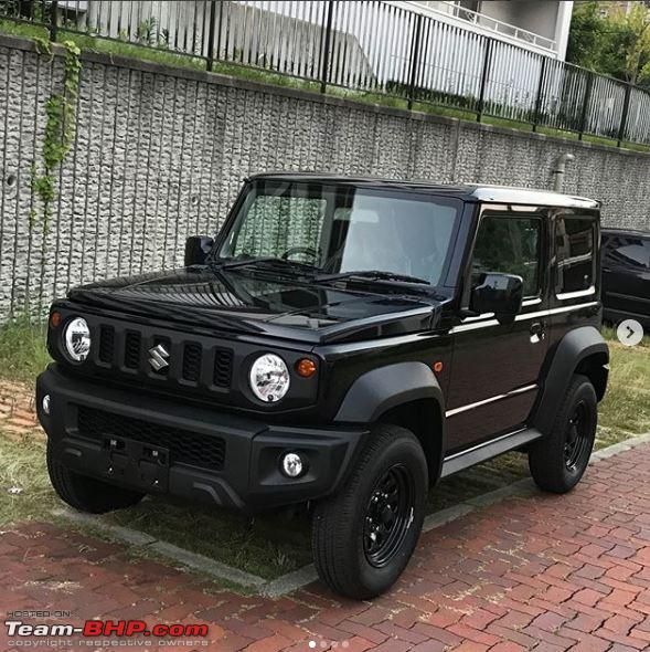 a black suzuki truck parked in front of a brick wall next to a sidewalk and fence