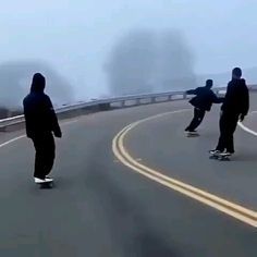 three skateboarders are riding down the road on a foggy day in winter