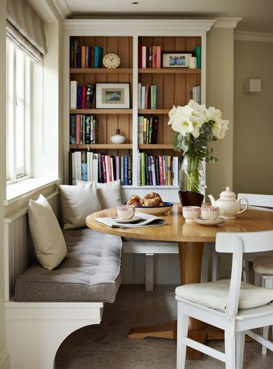 a dining room table with bookshelves in the background and two white chairs around it