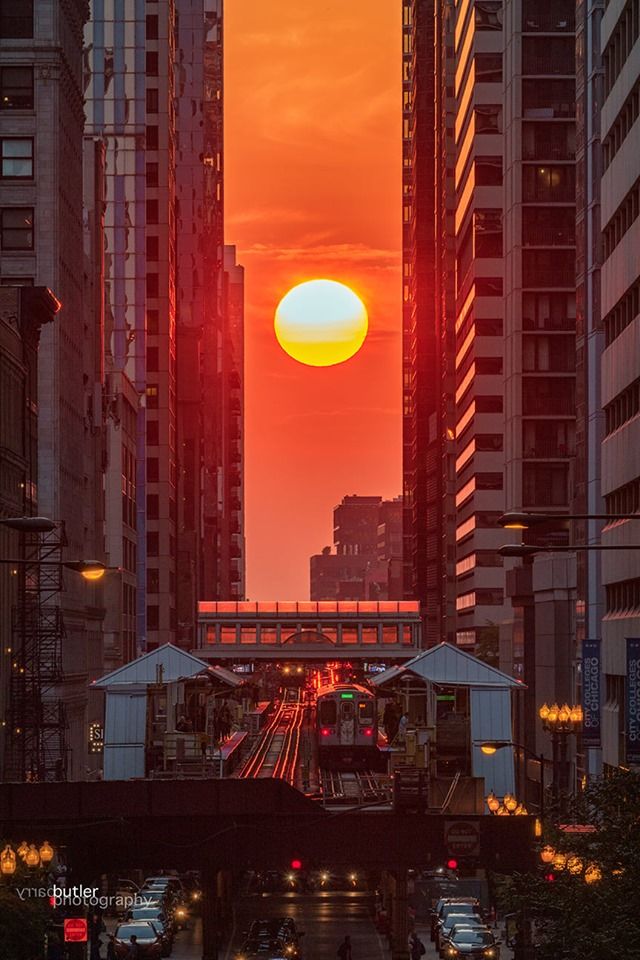 the sun is setting behind tall buildings and traffic on a city street with skyscrapers in the background